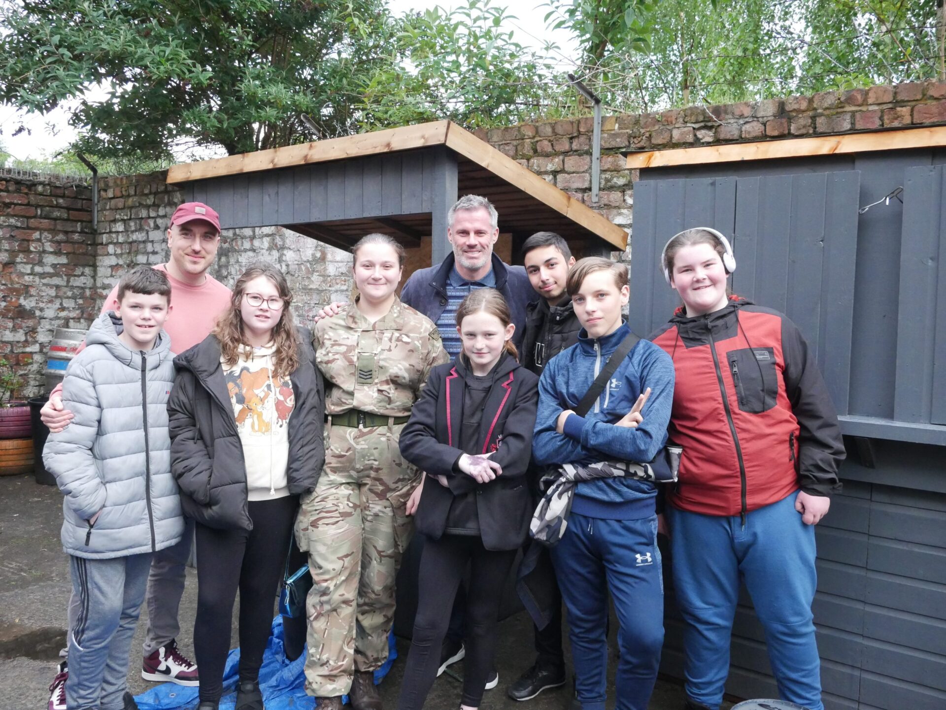 Group of children stood outside posing with two adults and a veteran