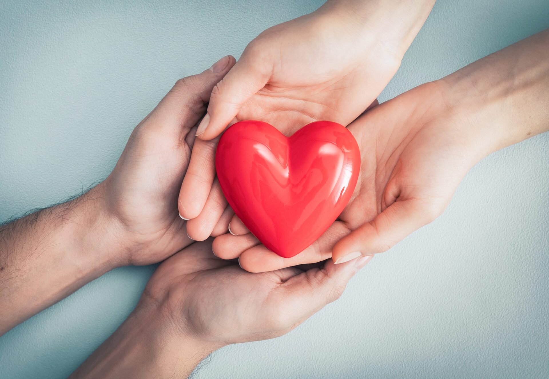 Two pairs of hands holding a love heart ornament